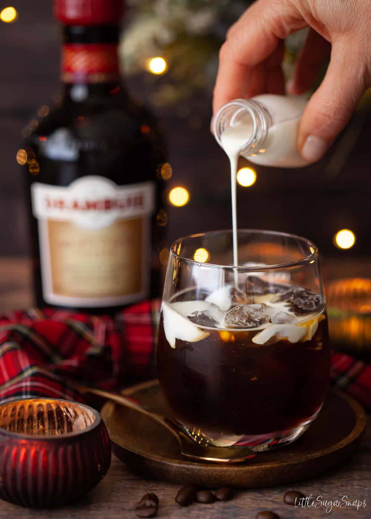 Cream being poured over a dark beverage in a glass filled with ice.