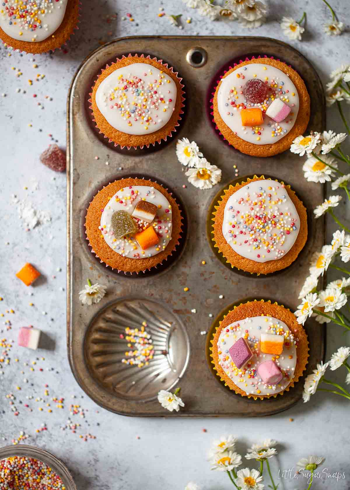 Iced fairy cakes in a vintage baking tin. They are decorated with sweets and sprinkles.