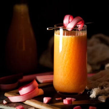 Rhubarb juice in a tall glass with a rhubarb curl garnish.