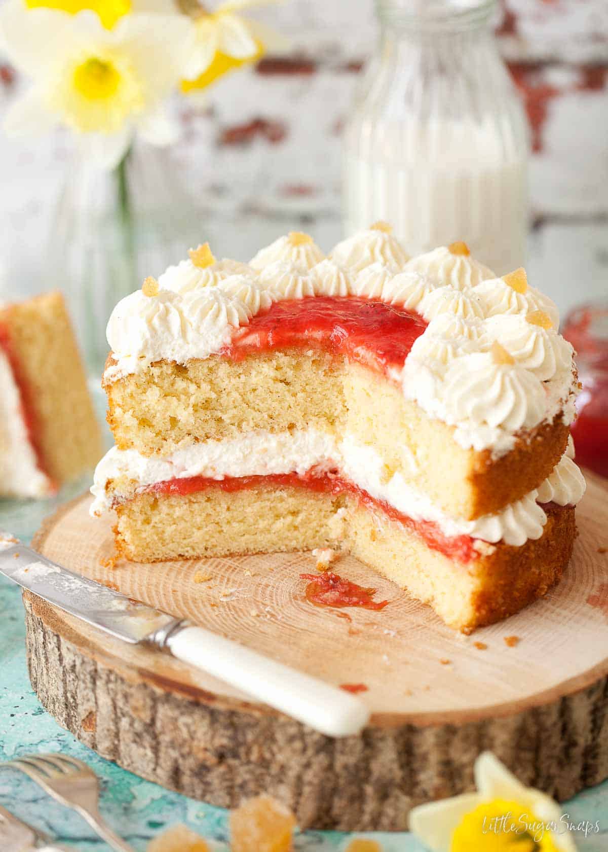 A small sponge cake filled with jam and cream with a few pieces cut from it.