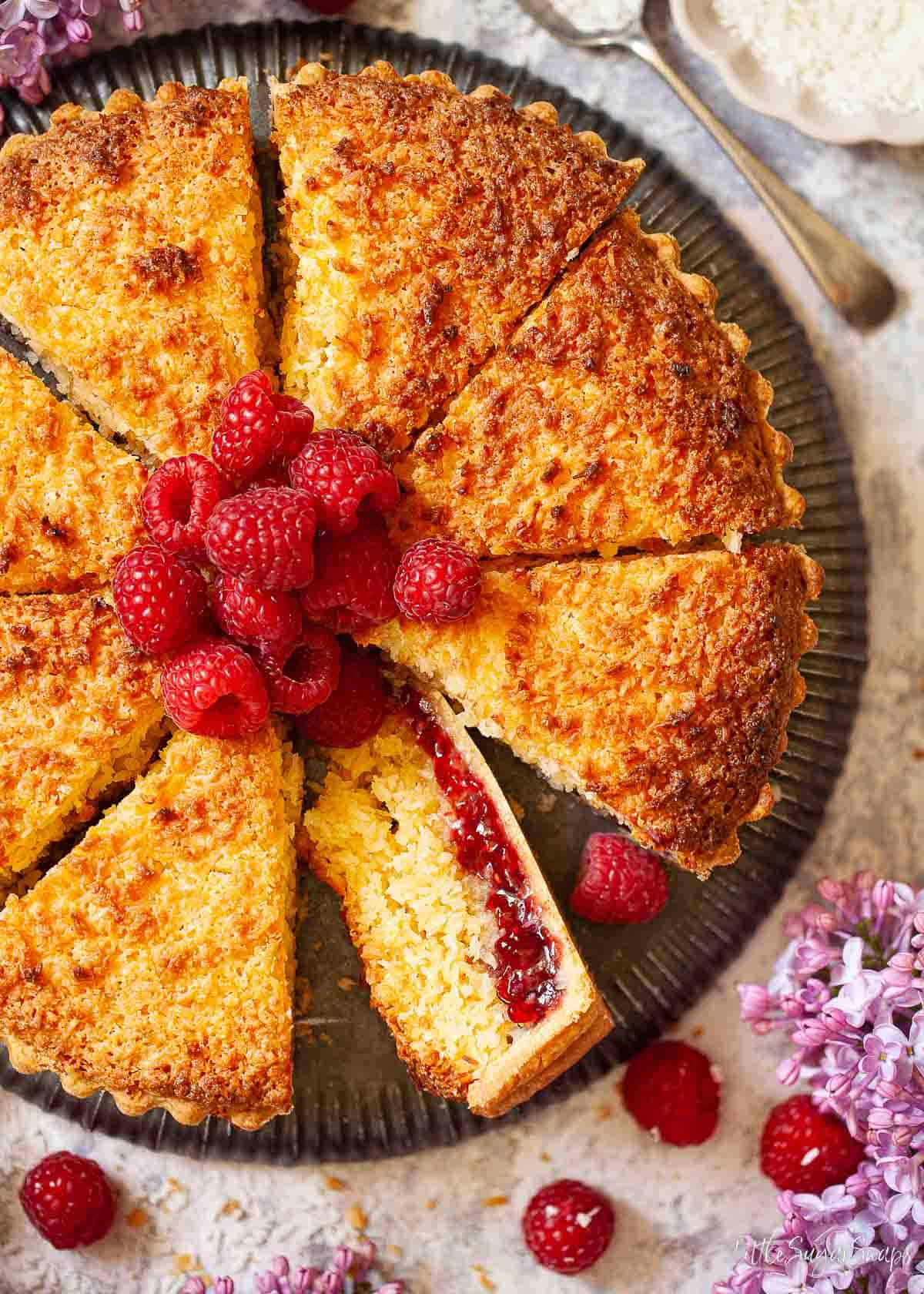 Close-up of a jam and coconut tart that has been cut into slices.