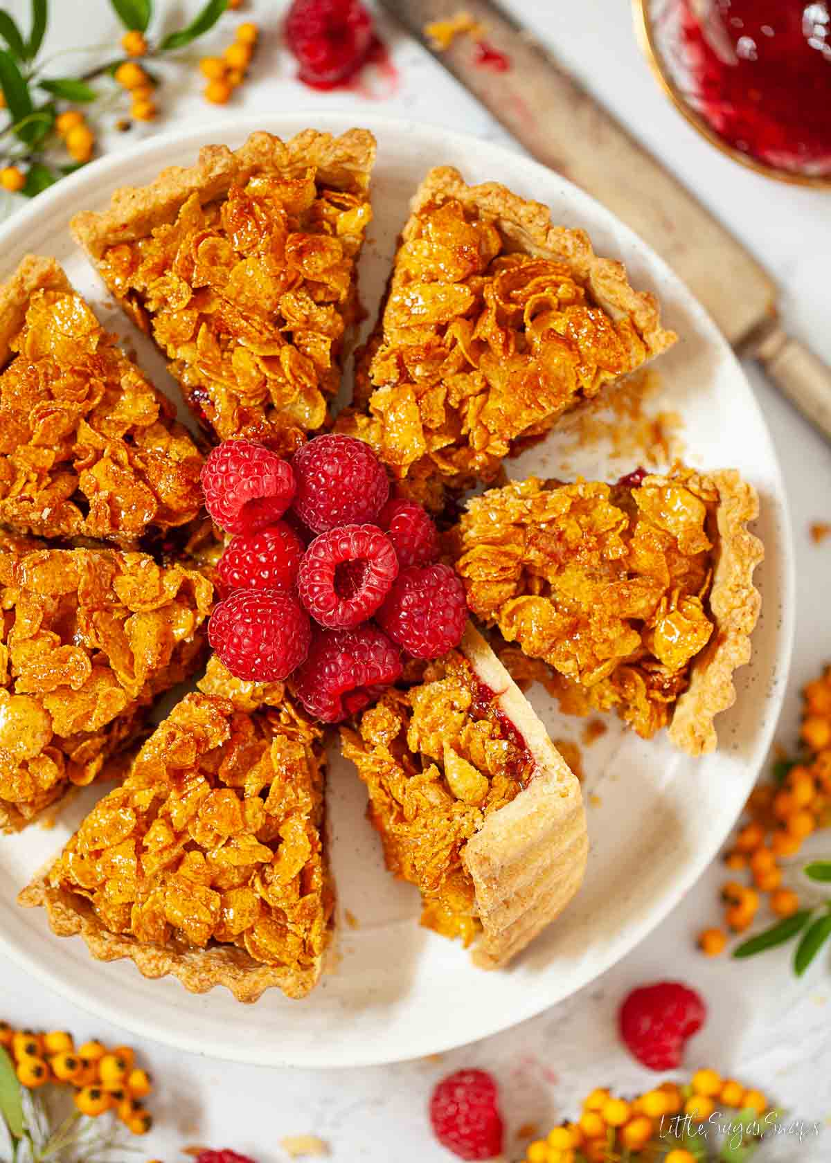 A cornflake tart with jam and fresh raspberries sliced and ready to serve.