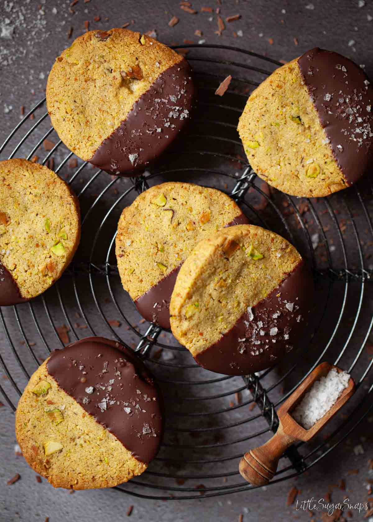 Chocolate dipped pistachio biscuits sprinkled with sea salt on a wire rack.