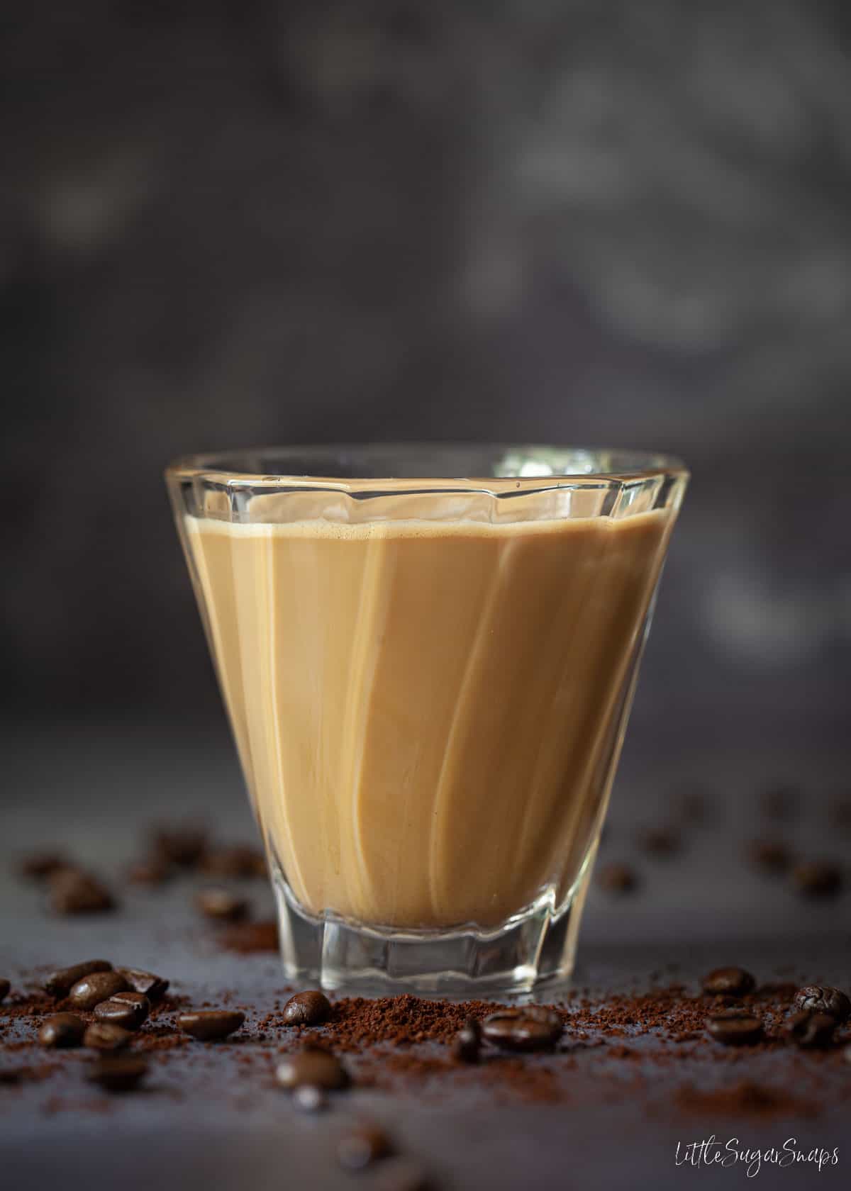 A single glass of Spanish latte surrounded by coffee beans.