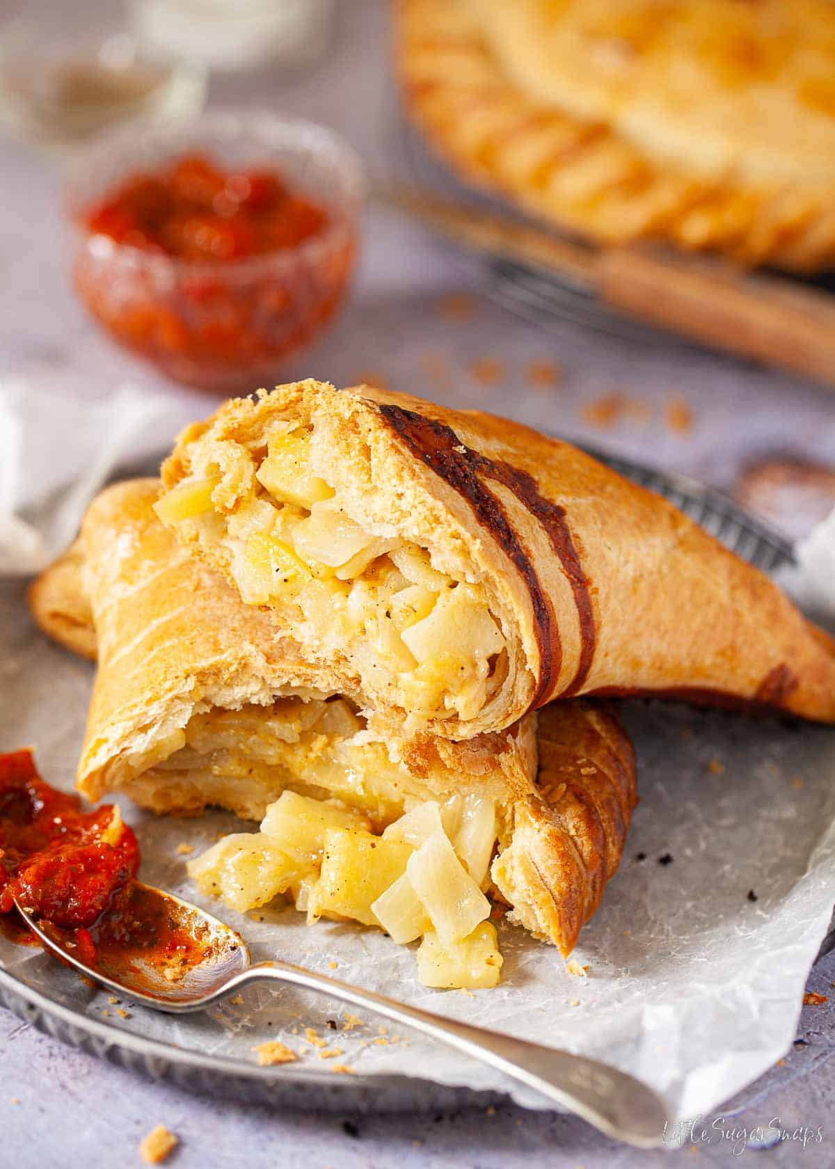 A potato, cheese and onion pasty torn open on a plate to reveal the filling.