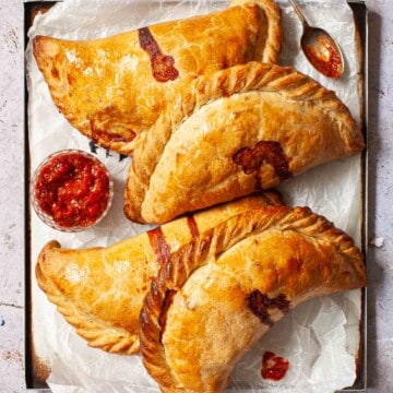 Four cheese and onion pasties on a baking sheet.