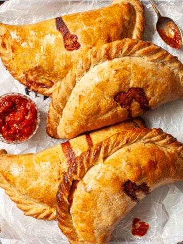 Four cheese and onion pasties on a baking sheet.