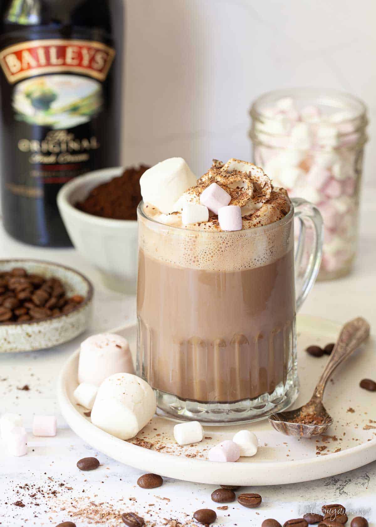 An Irish mocha with cream and marshmallow and a bottle of Baileys in the background.