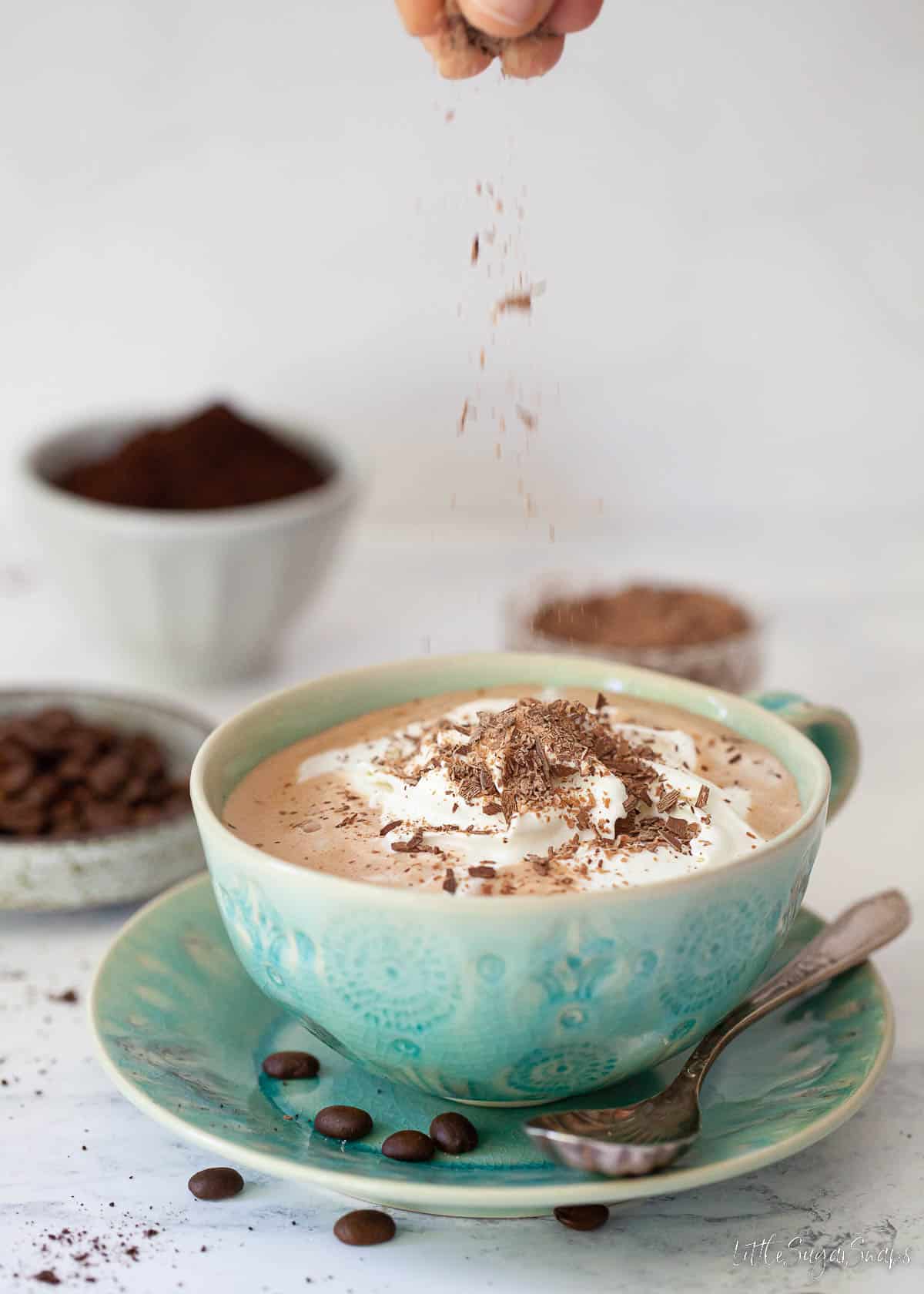 Chocolate flakes being sprinkled over a mug of Baileys mocha latte topped with cream.