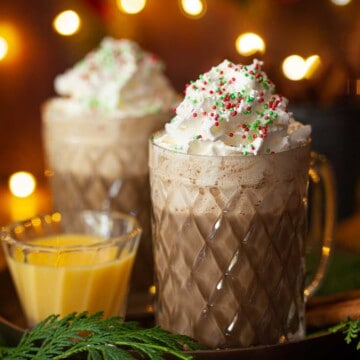 Two glass mugs filled with Christmas coffee and topped with whipped cream and sprinkles.