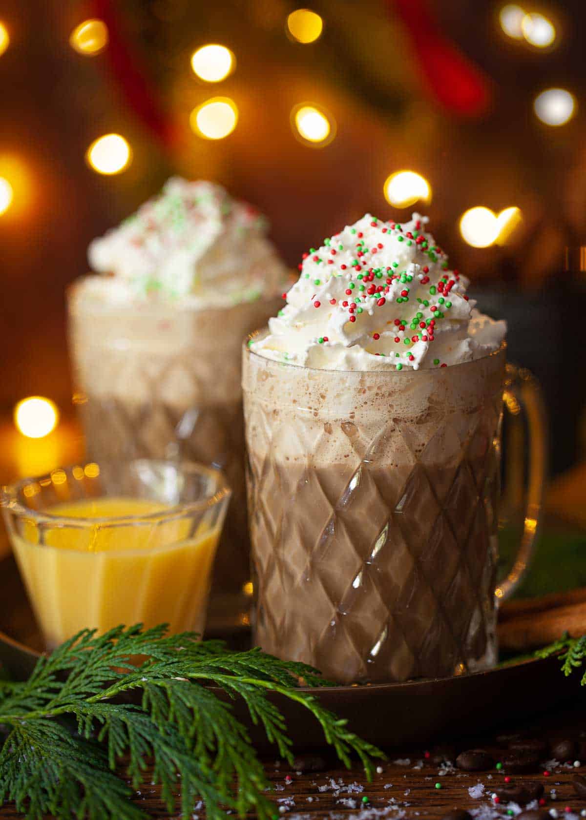 Two glass mugs filled with Christmas coffee and topped with whipped cream and sprinkles.