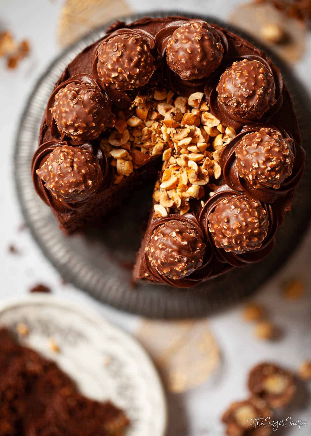 A Ferrero Rocher Cake topped with hazelnuts and chocolates with a slice cut out