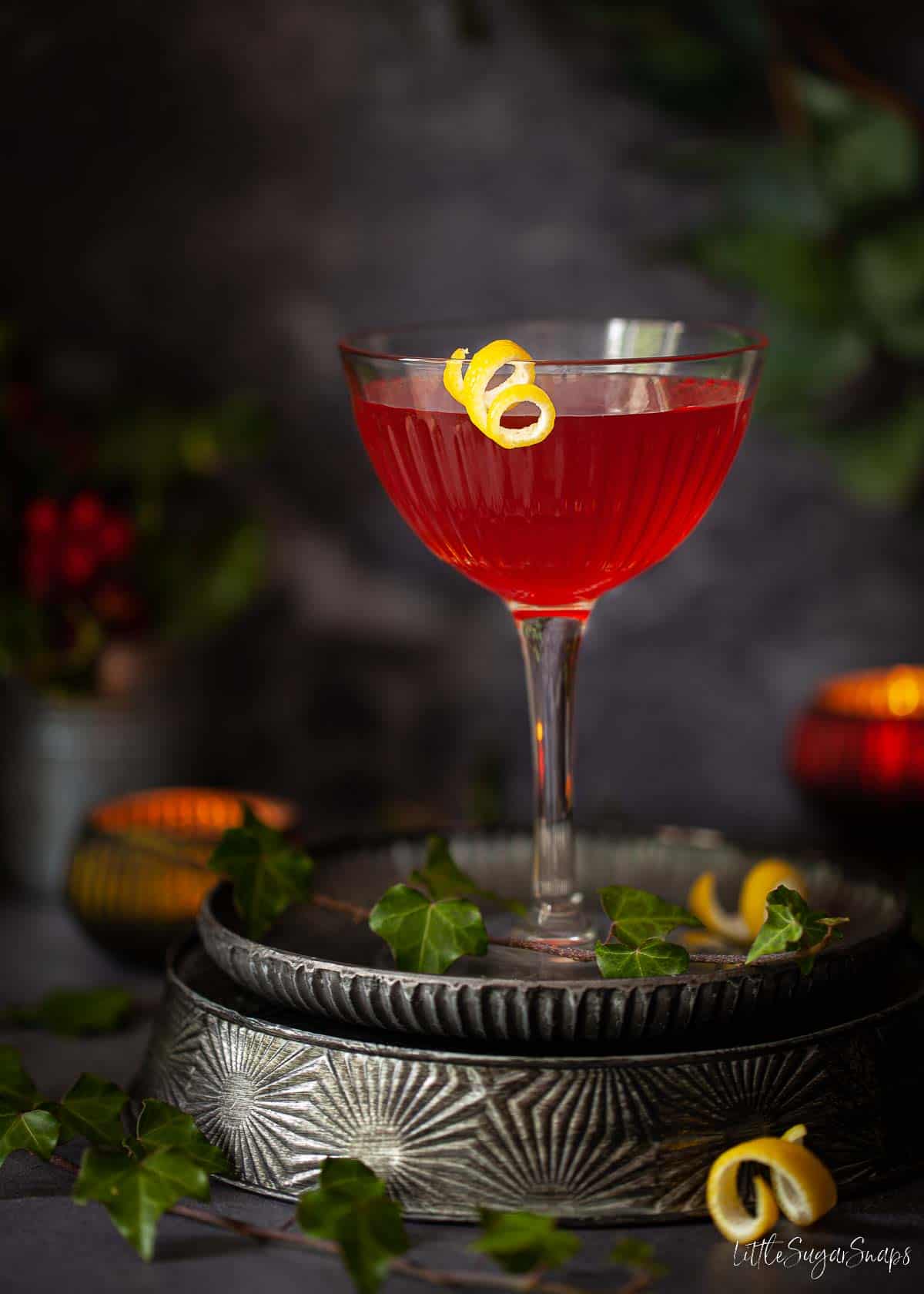 A red cocktail made with Italian bitters presented in a coupe glass with a lemon garnish.