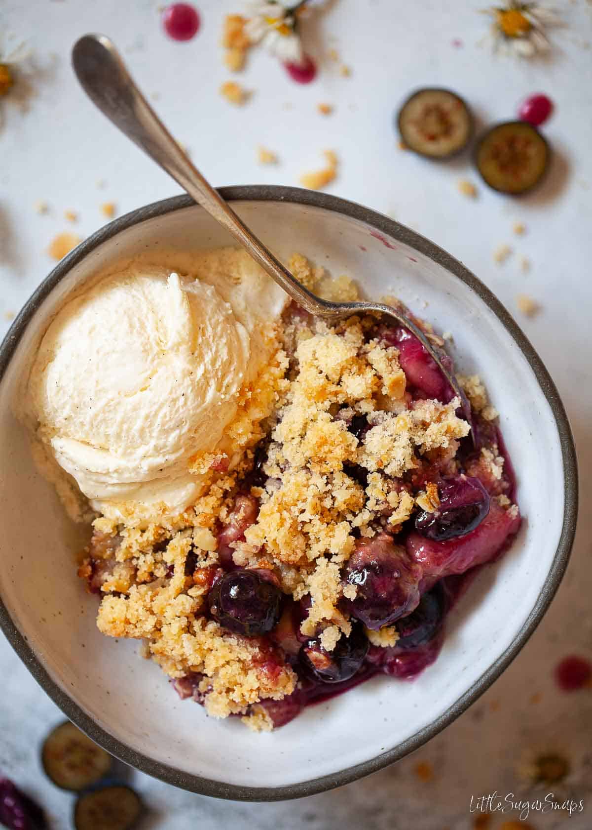 Apple and Blueberry crumble in a bowl with a scoop of ice cream.