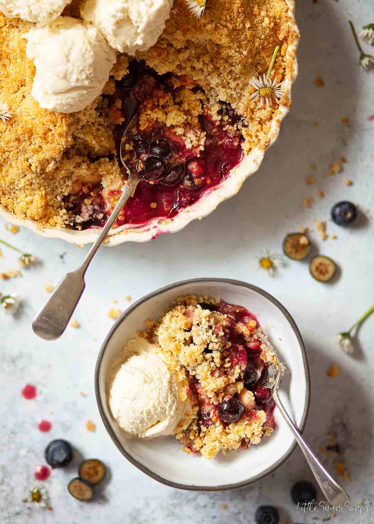 Apple and blueberry crumble being served in a bowl with ice cream.