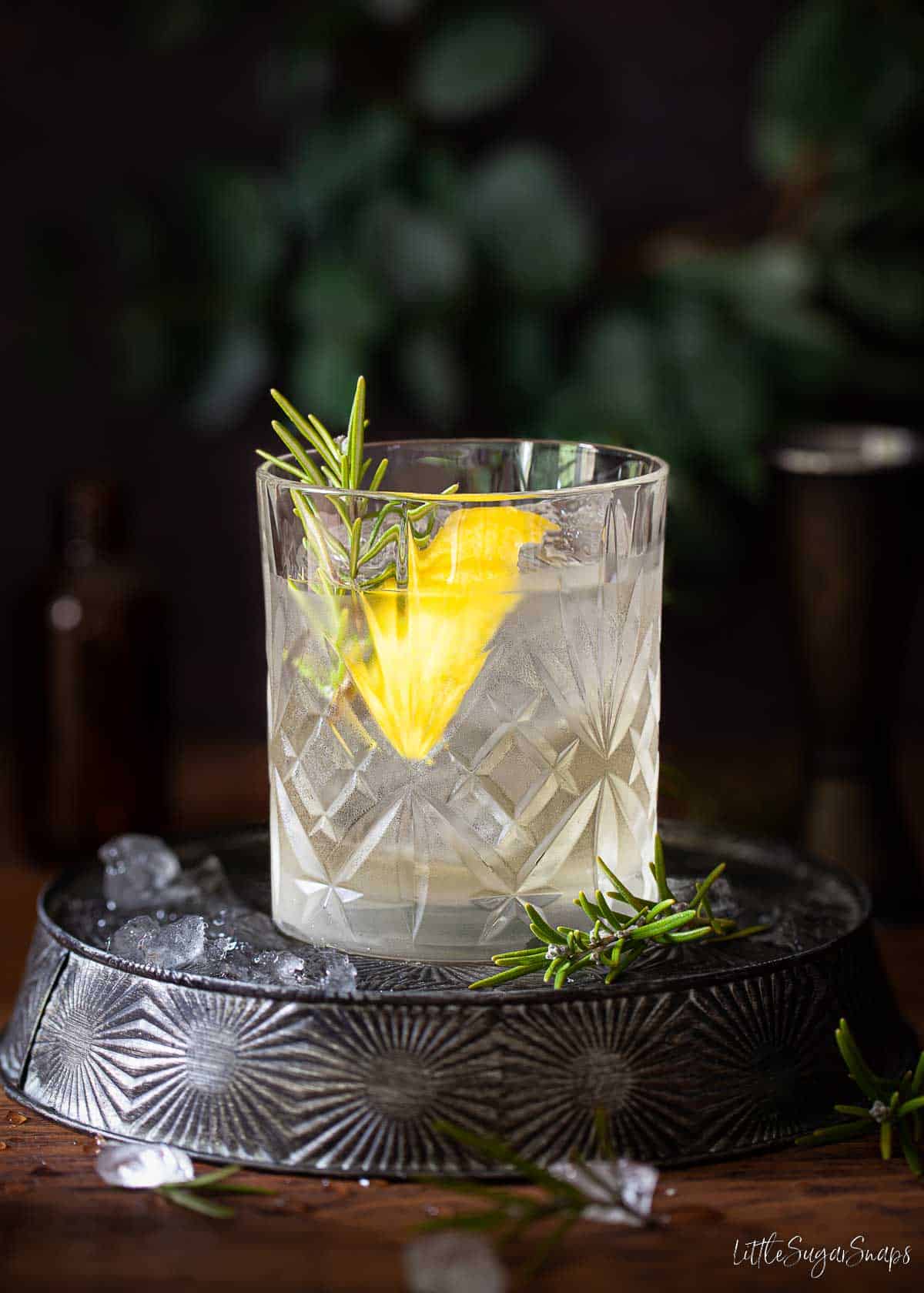 A white negroni in a tumbler garnished with lemon and rosemary.