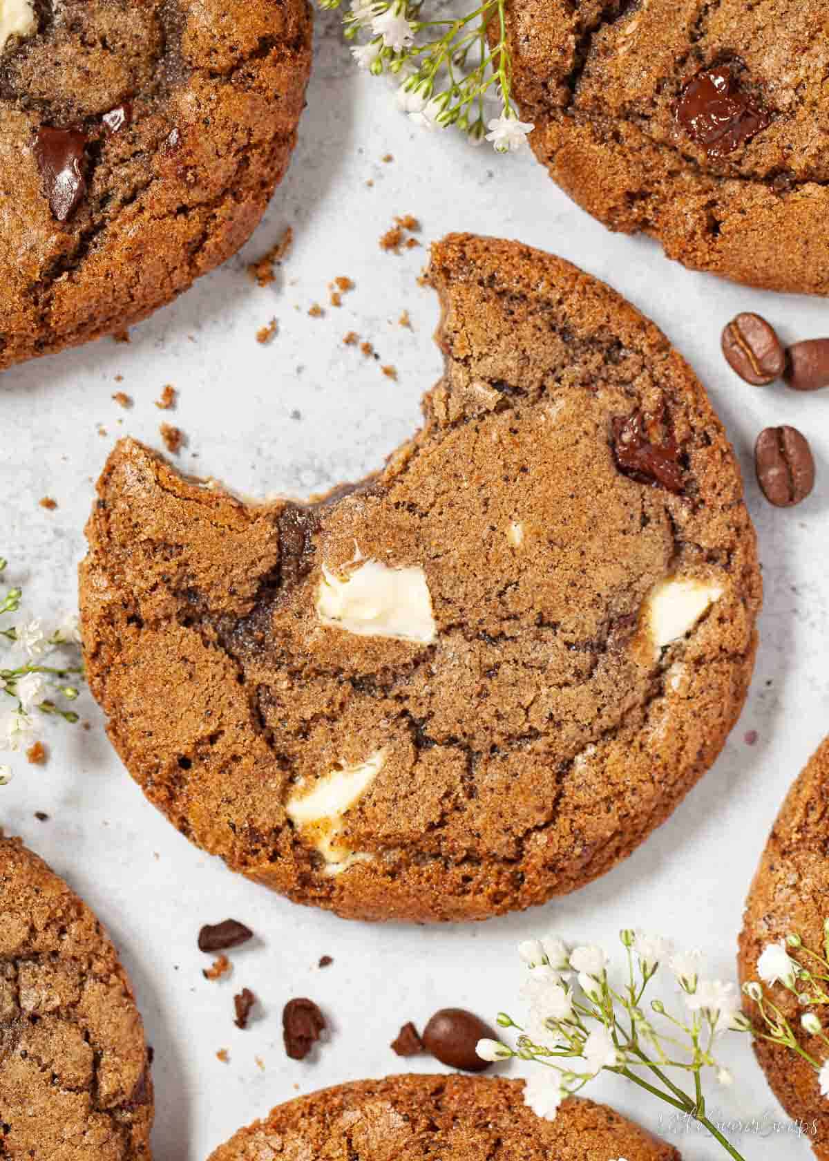 Chocolate chip coffee cookies on a worktop and one has a bite taken from it.