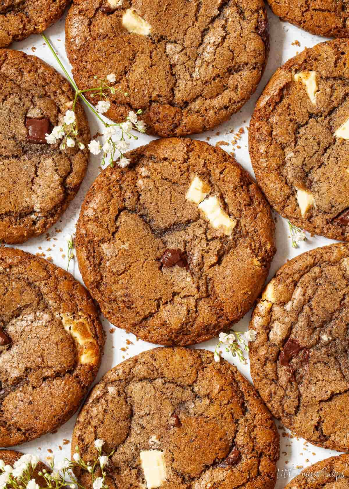 Chocolate chip and coffee cookies arranged on a worktop with white flowers.