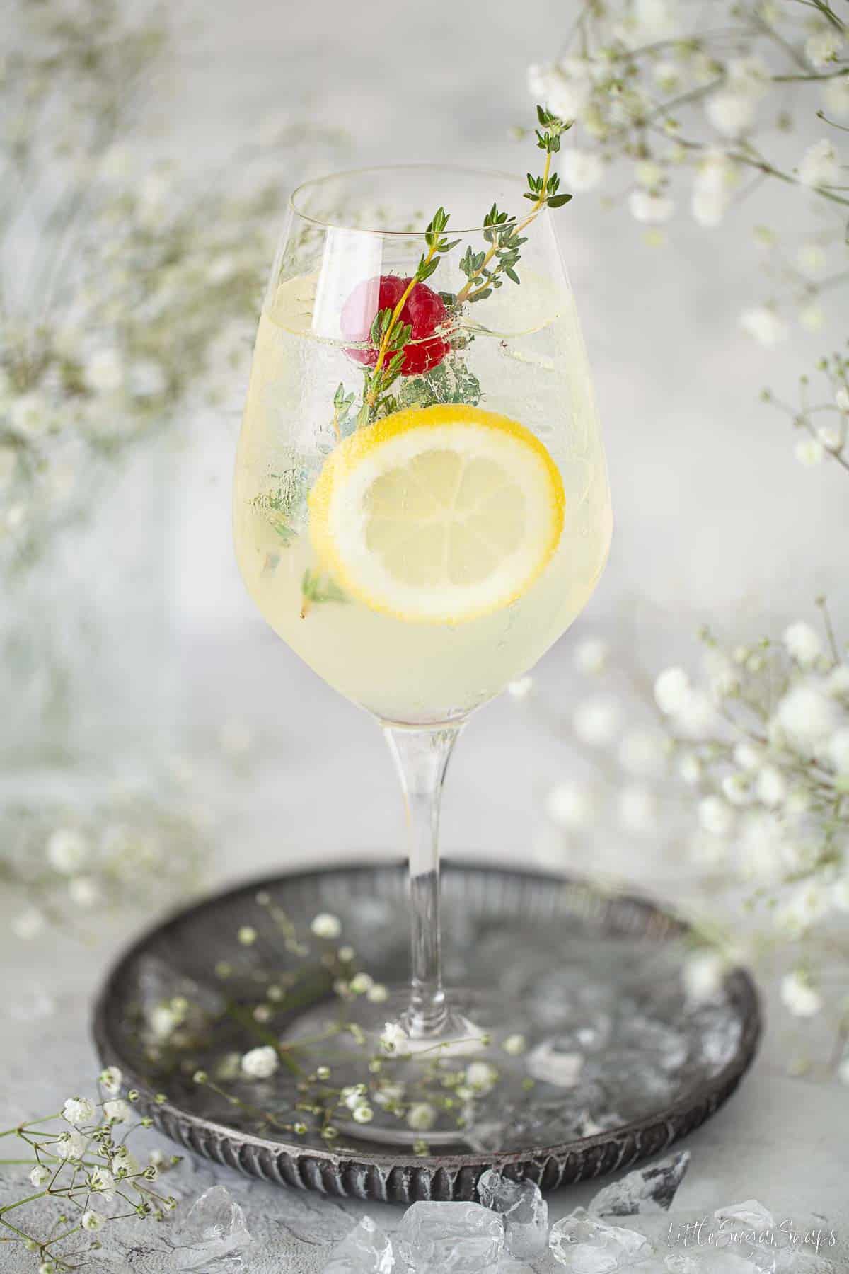 Wine glass holding a limoncello spritz cocktail with raspberry and thyme.