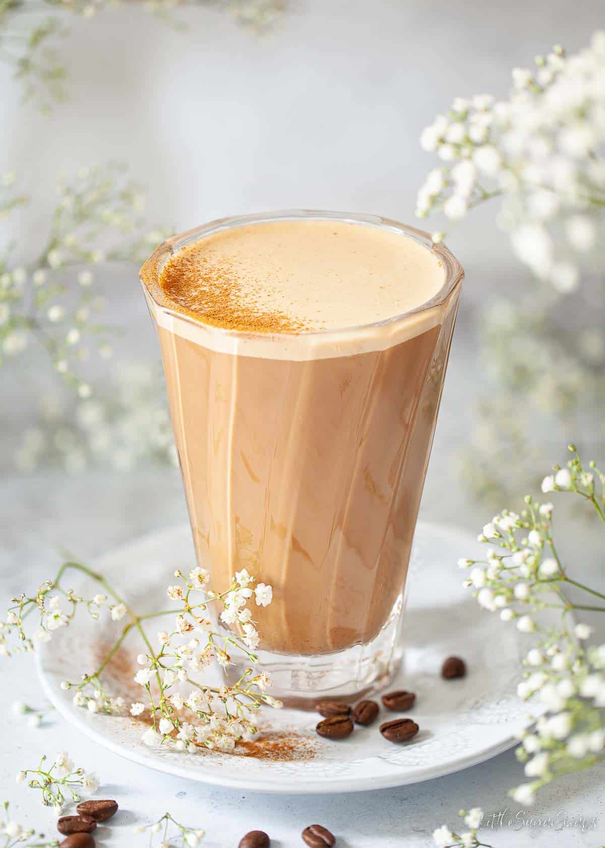 Honey latte presented in a modern coffee glass dusted with ground cinnamon.