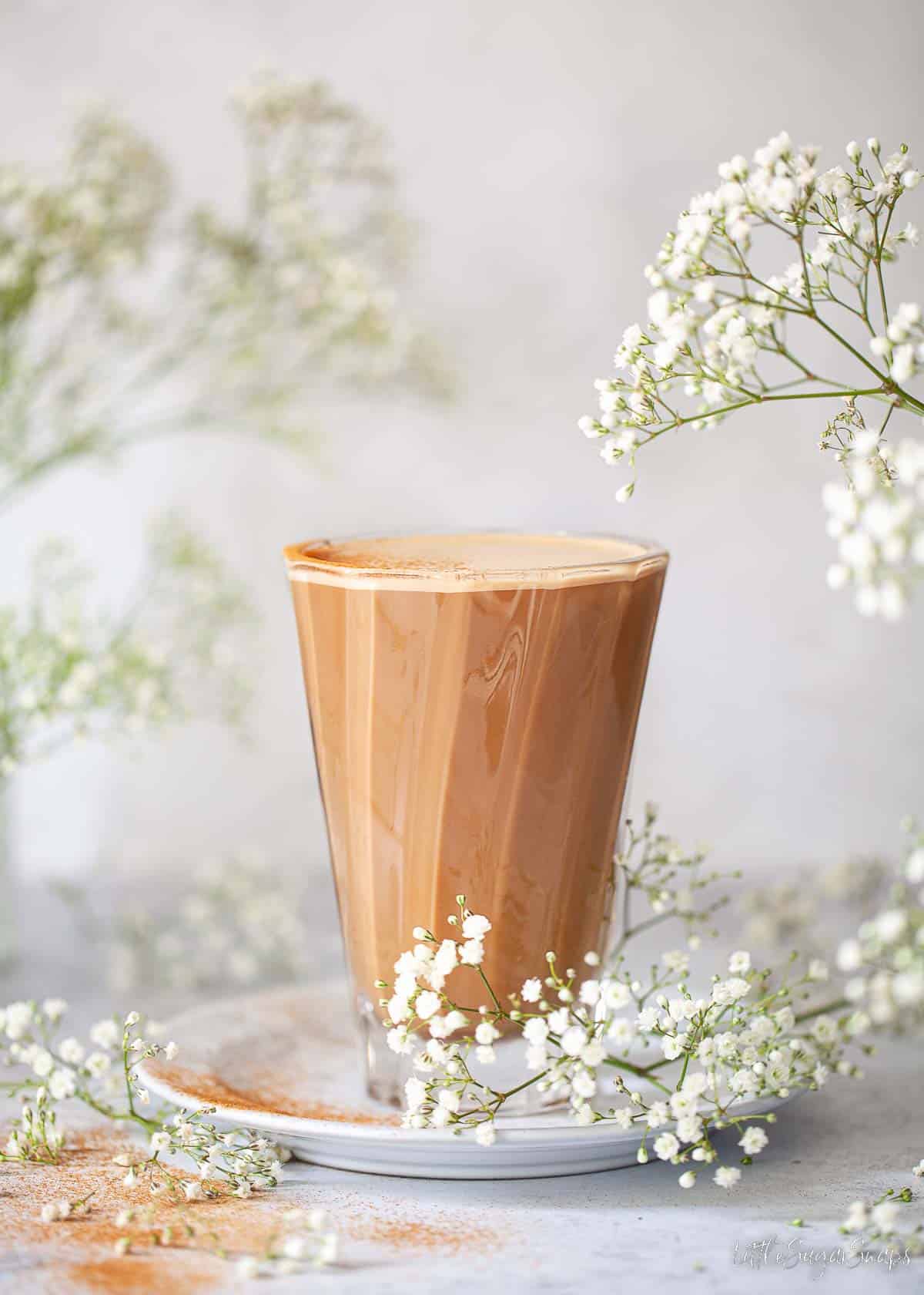 Oat milk latte in a modern coffee glass served with a dusting of ground cinnamon.