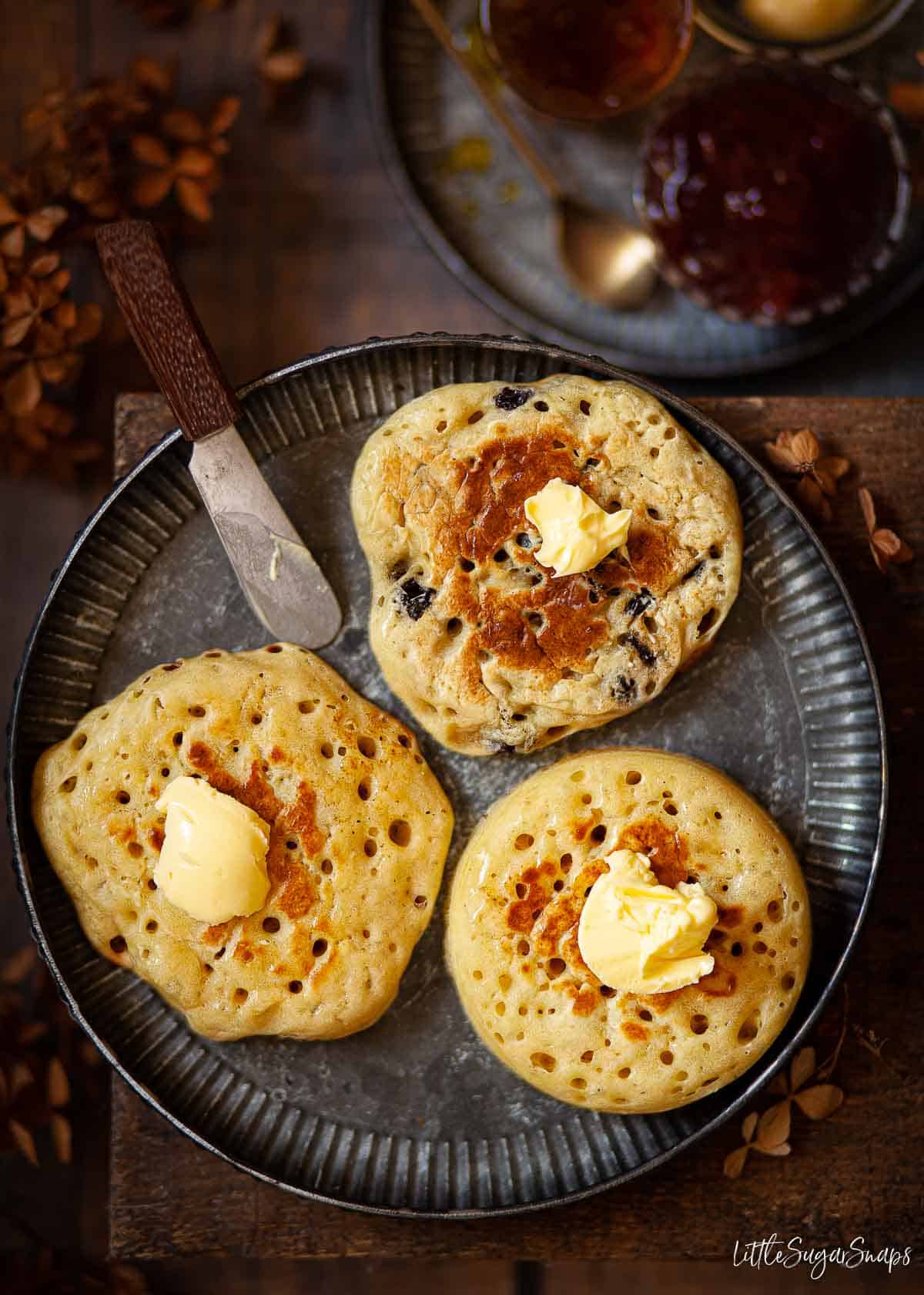 A mixture of griddle bread on a plate including a pikelet, a crumpet and a fruit pikelet.