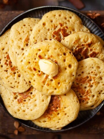 Close-up of pikelets on a plate with one on top with butter on it.