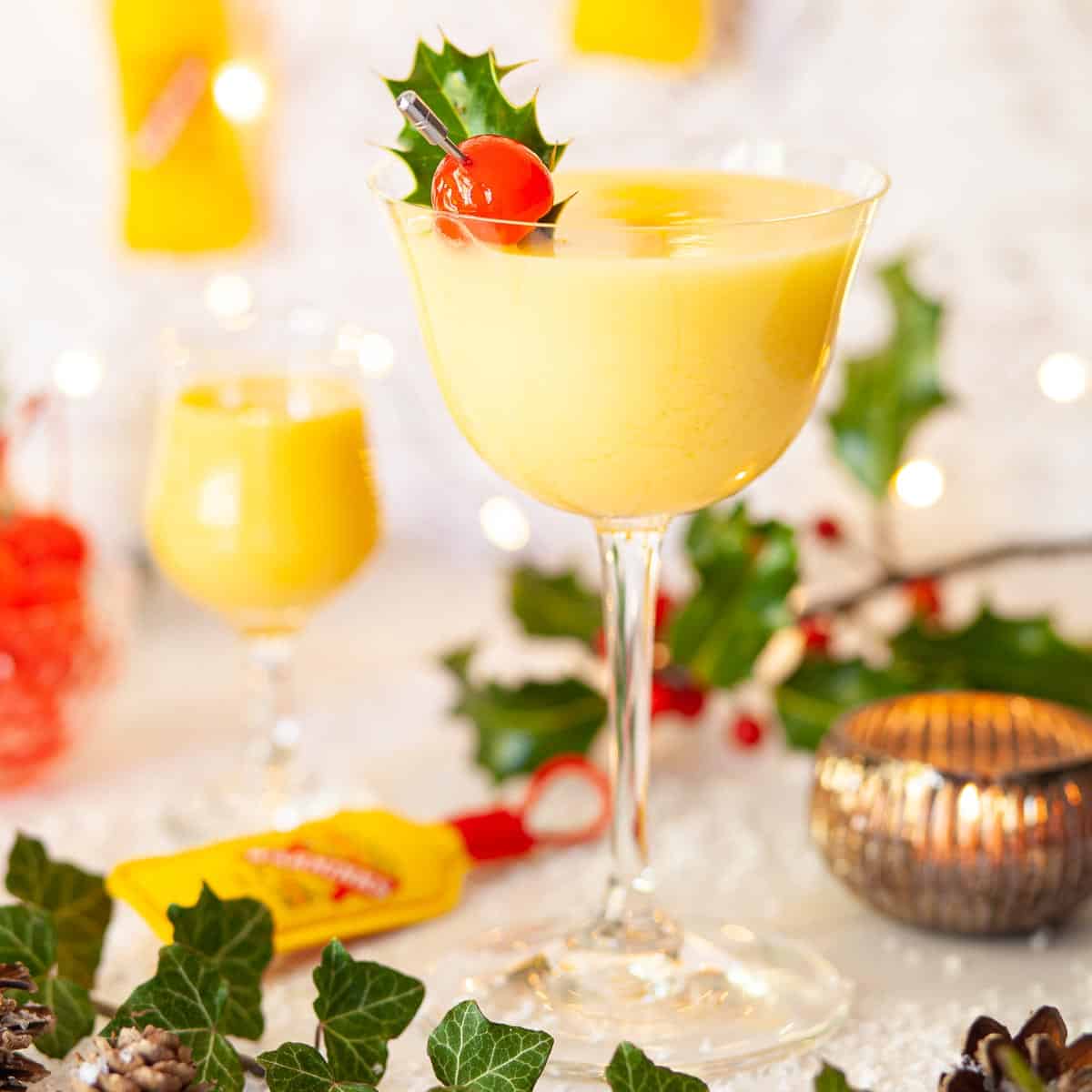 A snowball in a stemmed glass with a cocktail cherry garnish.