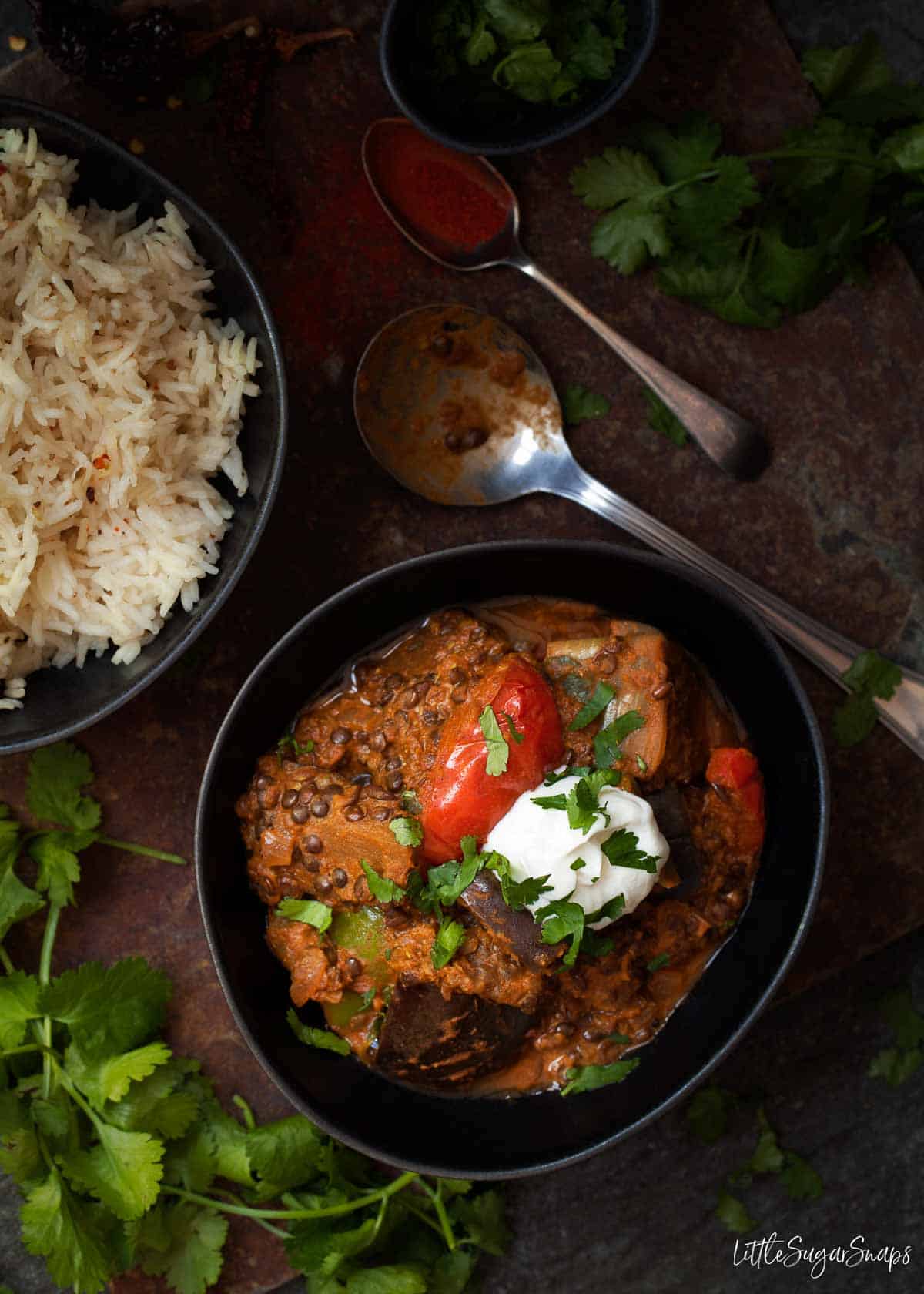 Aubergine and black lentil curry in a bowl and garnished with yoghurt and coriander.