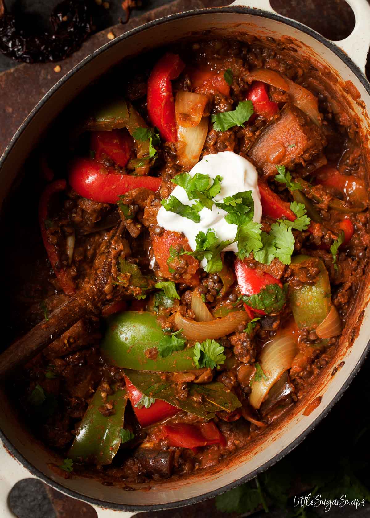 A cast iron cooking pot holding vegetarian rogan josh curry garnished with yoghurt and coriander.