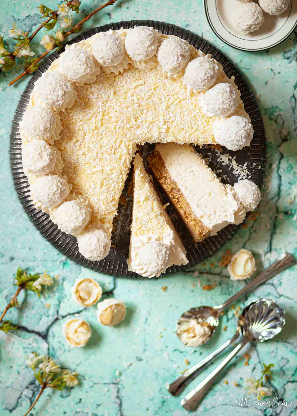 A Raffaello cheesecake partially cut. Two slices are ready to be served.