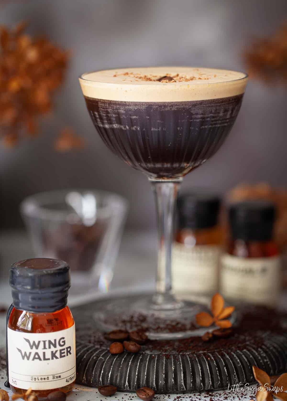 An espresso martini cocktail with small bottles of rum alongside it.