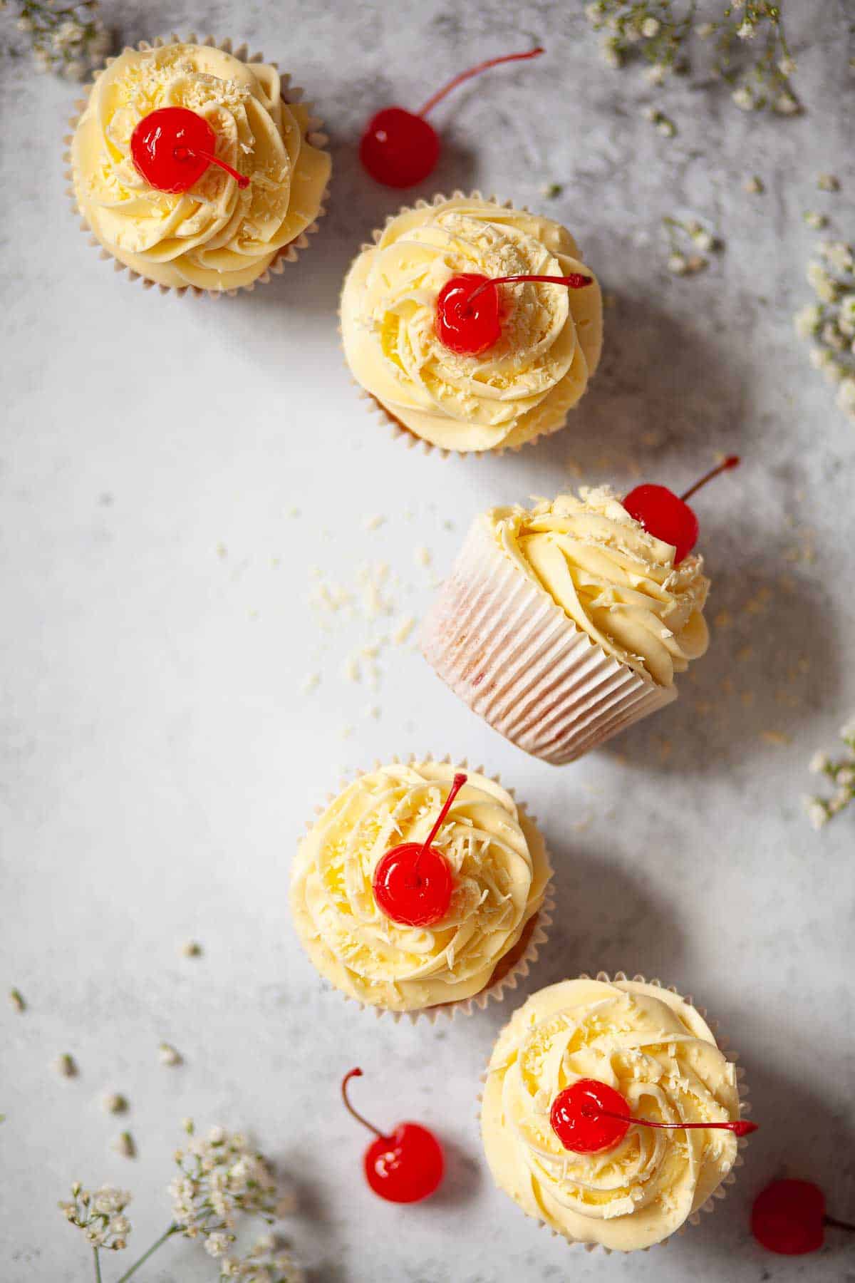 Cakes on a worktop decorated with piped buttercream, grated white chocolate and a stemmed cherry.