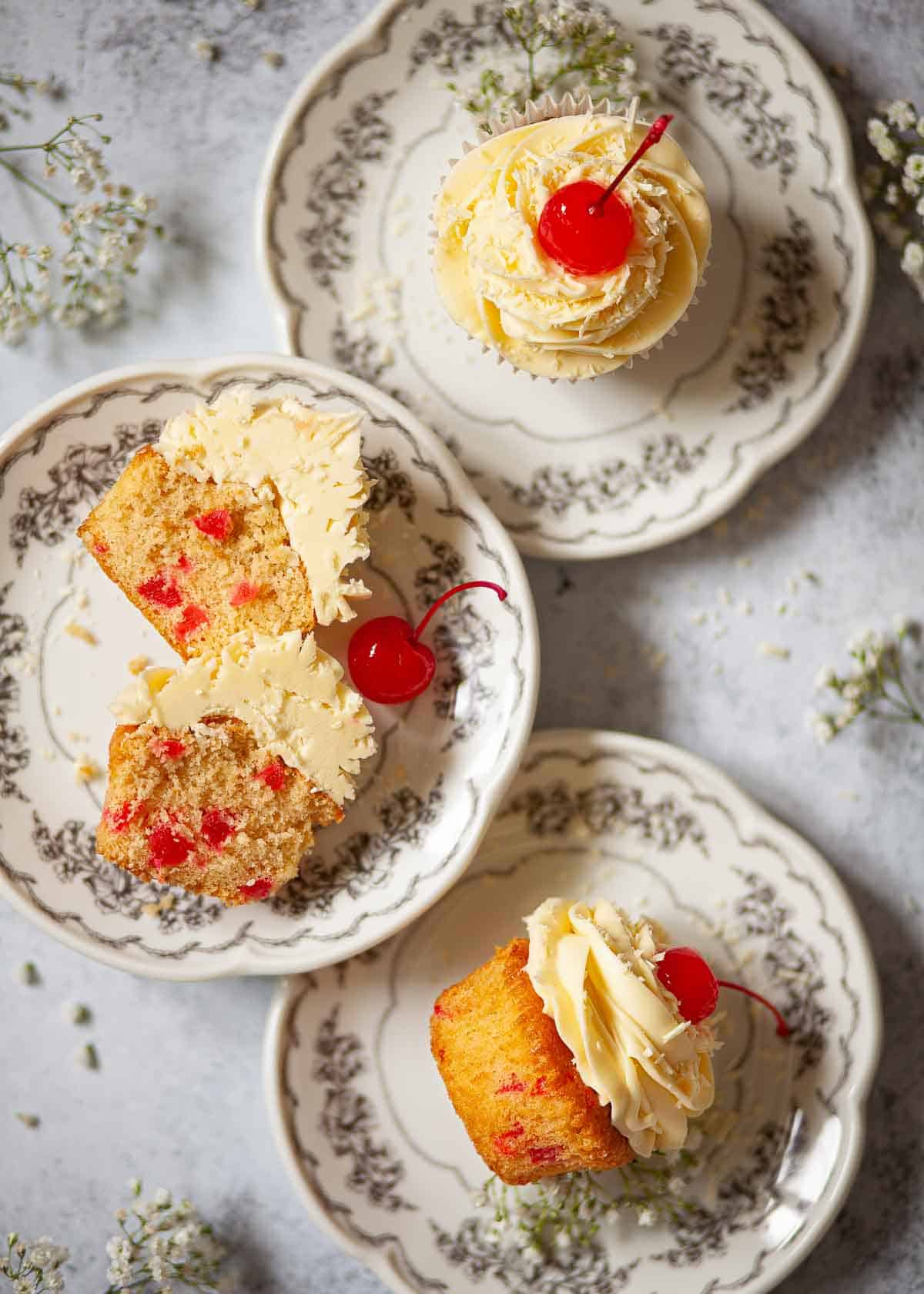 Cherry cupcakes on plates with one cut in half to reveal chopped cherries in the sponge cake.