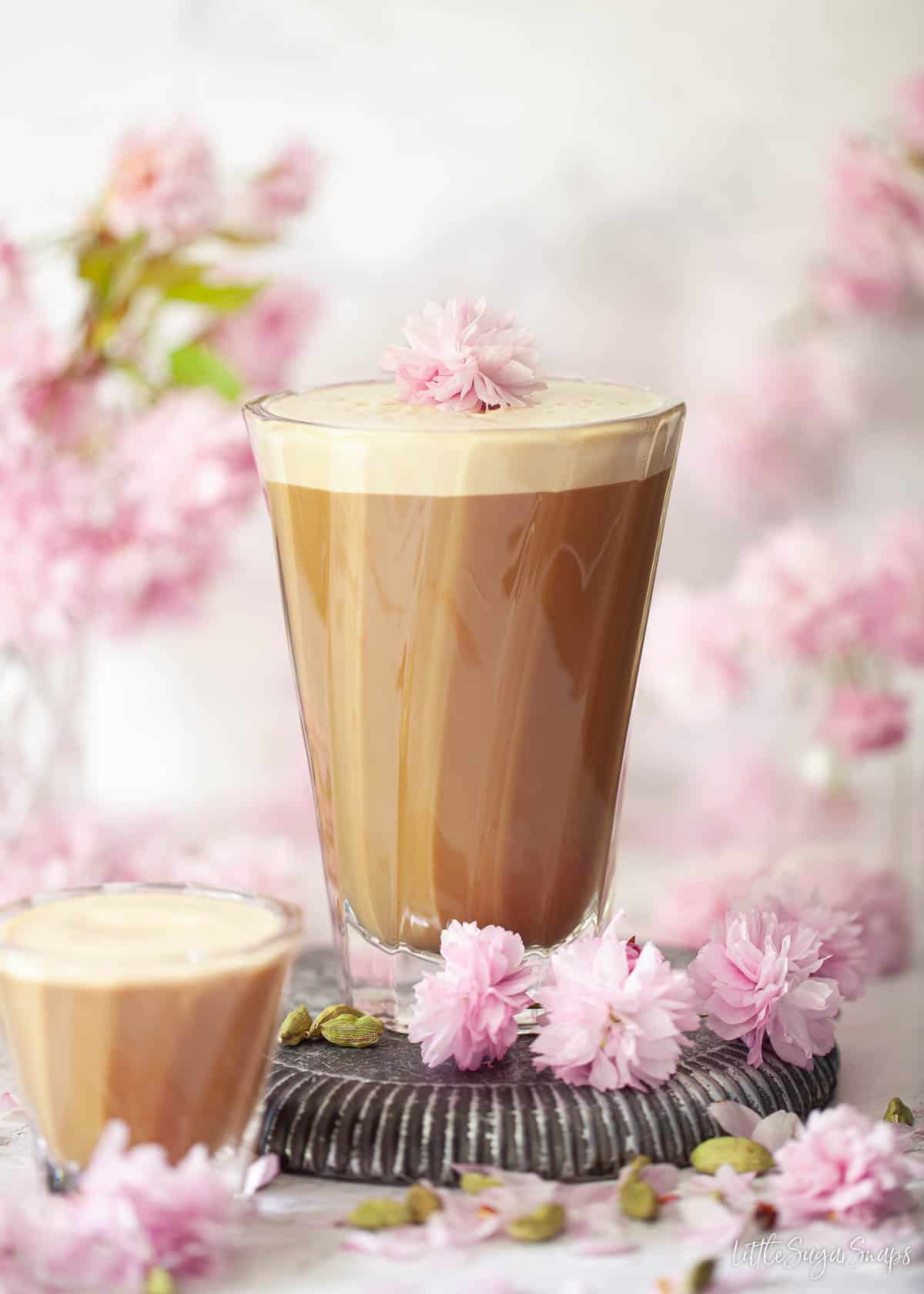 A tall glass of almond milk latte garnished with pink blossom.