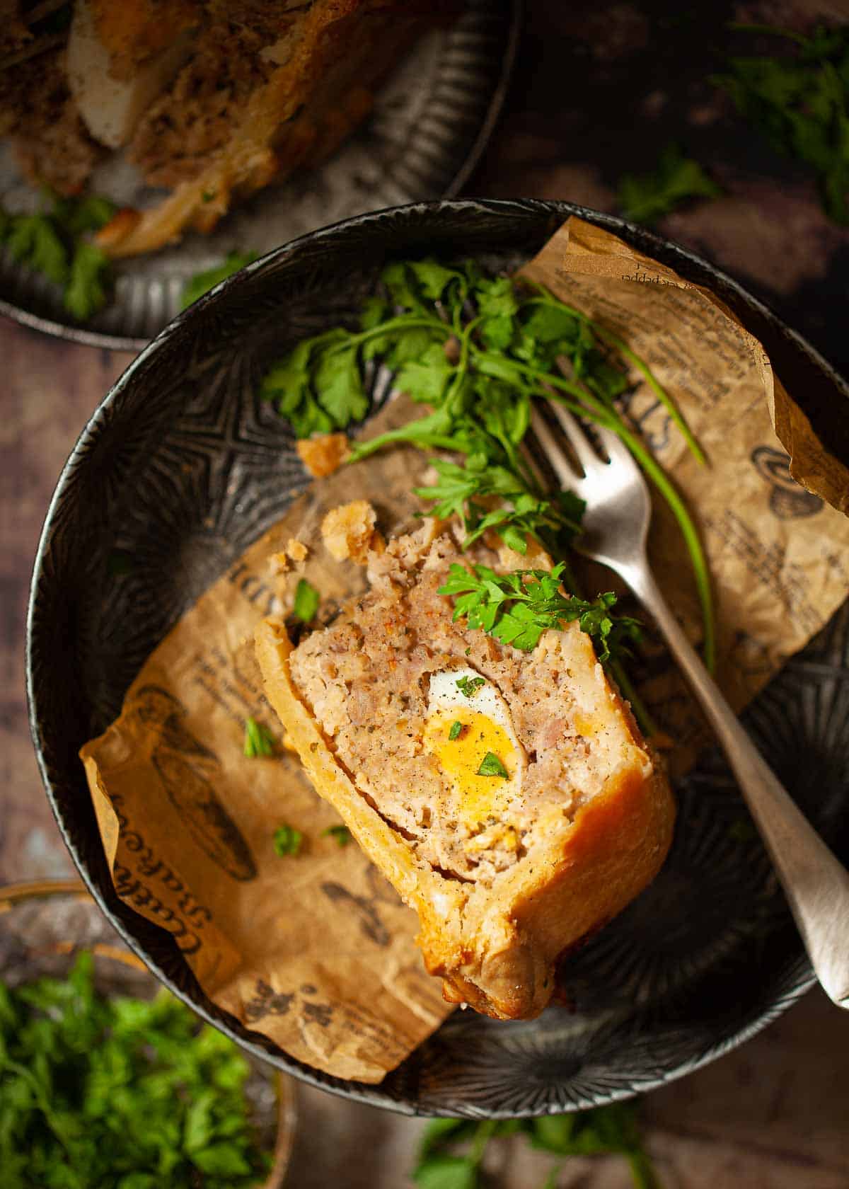 A slice of sausage and egg pie on a tin dish with parsley garnish.