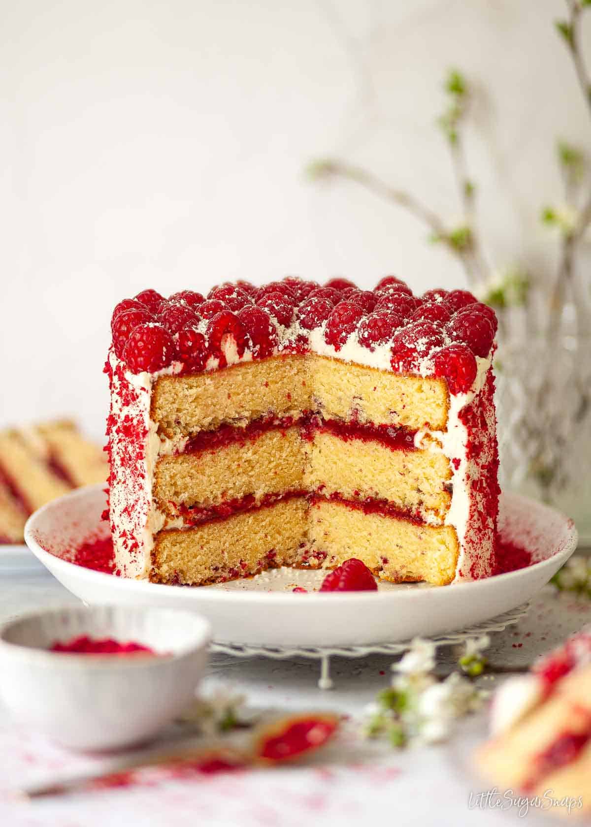 A frosted white chocolate and raspberry cake with several slices cut out of it.