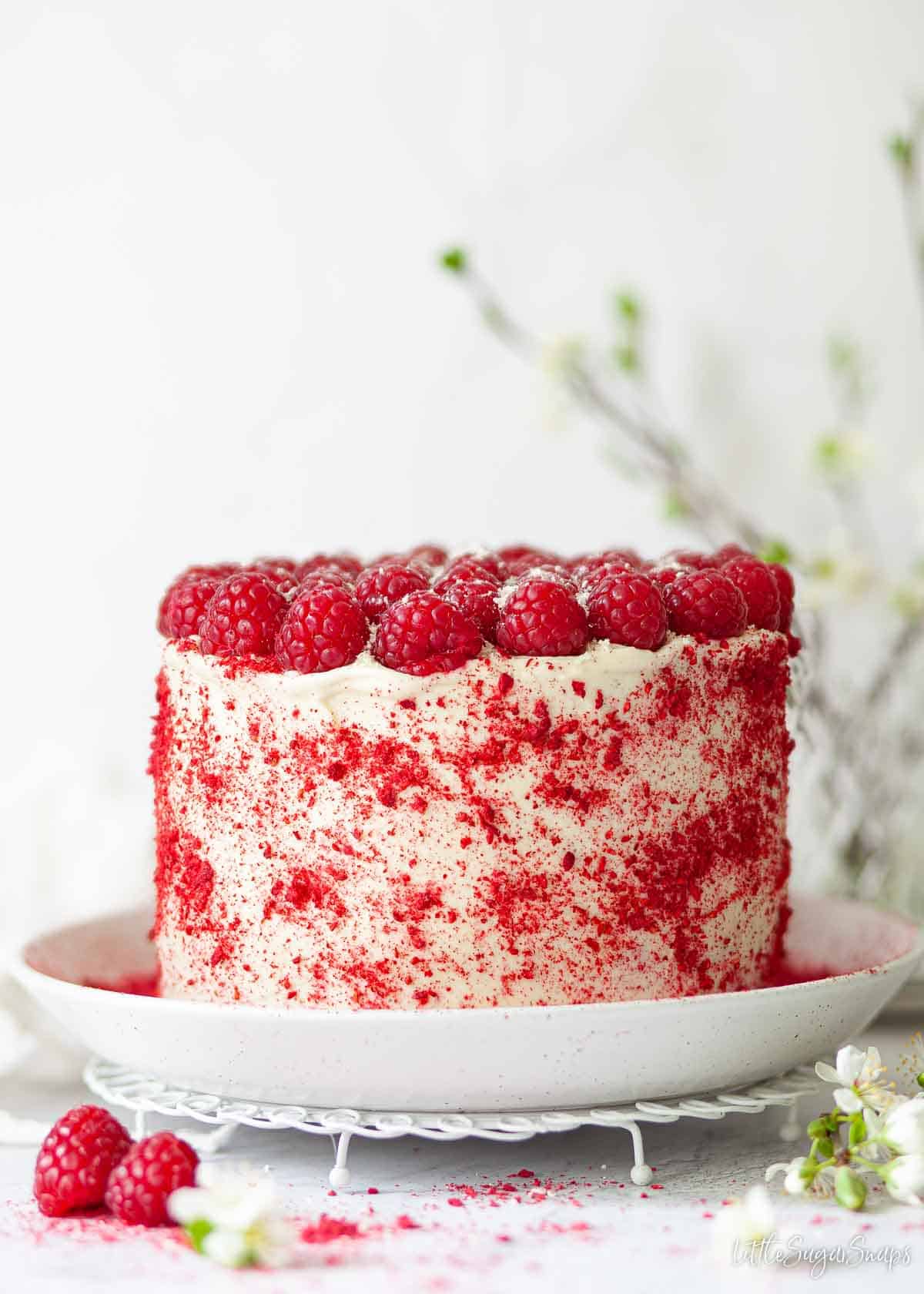 A frosted raspberry layer cake decorated with fresh raspberries and crushed freeze-dried raspberries.