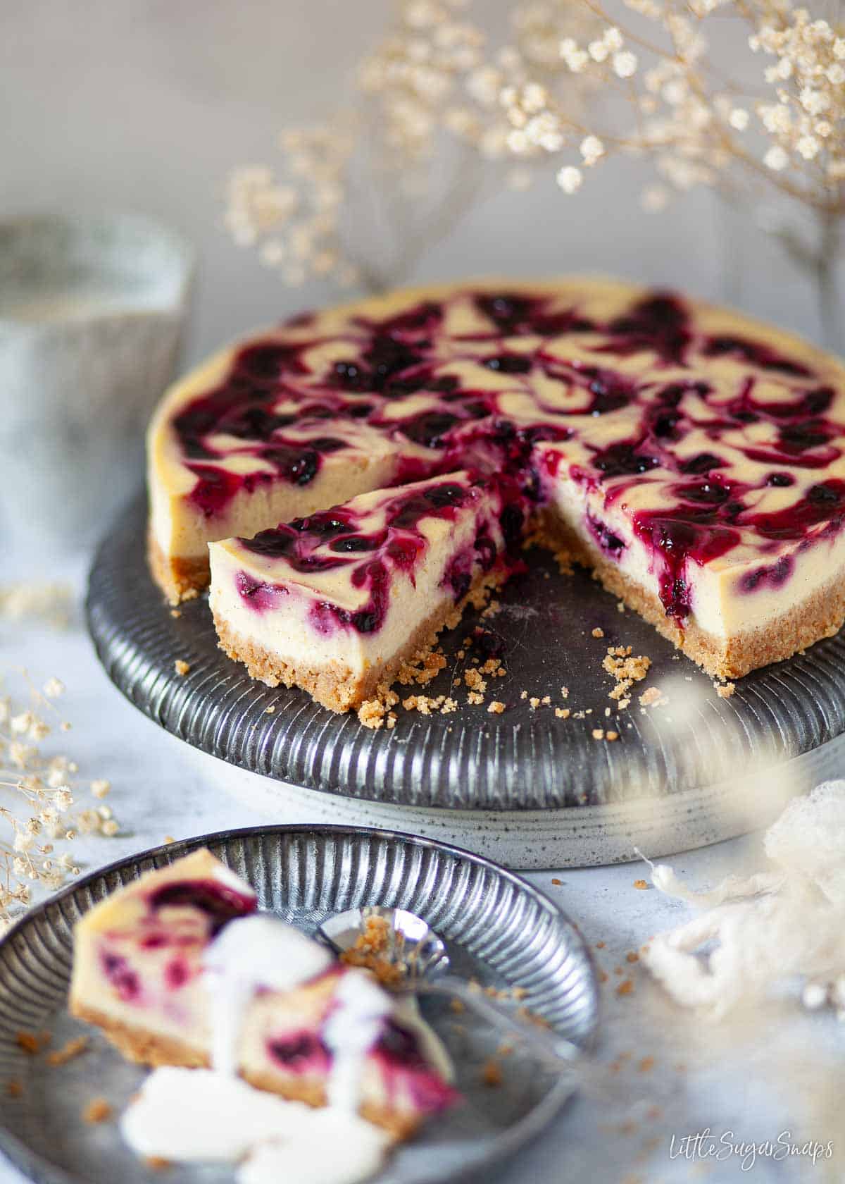 Baked blackcurrant cheesecake with slices cut and one on a plate with cream on top.