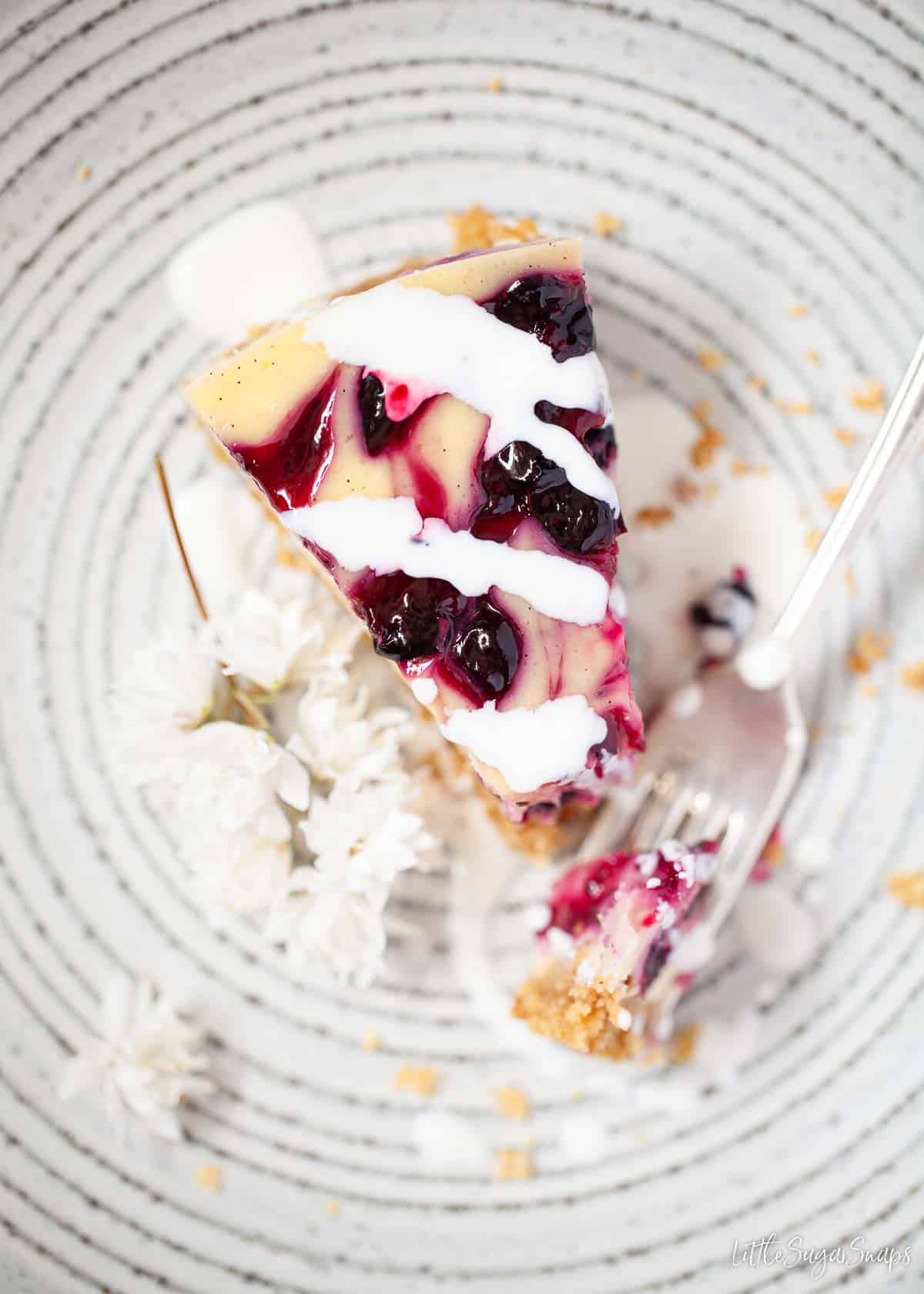 A slice of blackcurrant cheesecake served with cream with a fork alongside.