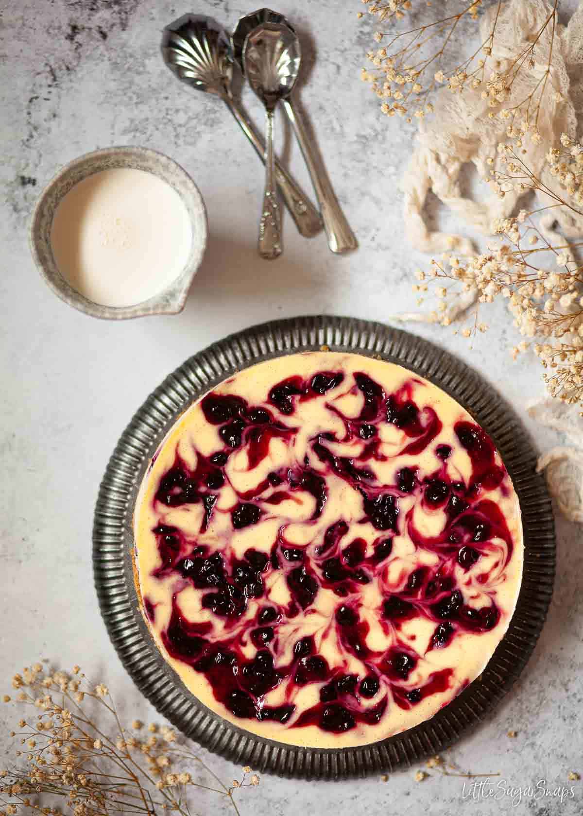 A marbled blackcurrant cheesecake on a plate with a jug of pouring cream at the side.