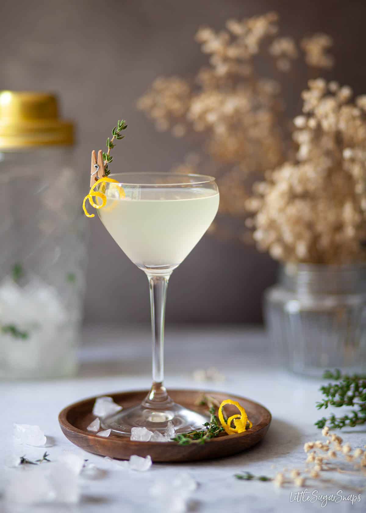 A limoncello martini garnished with lemon zest spiral and fresh thyme sprig.