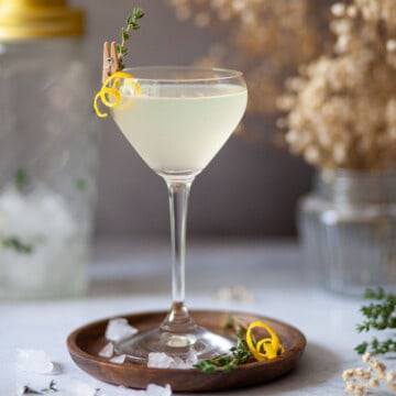 Limoncello martini garnished with a lemon zest spiral and fresh thyme.