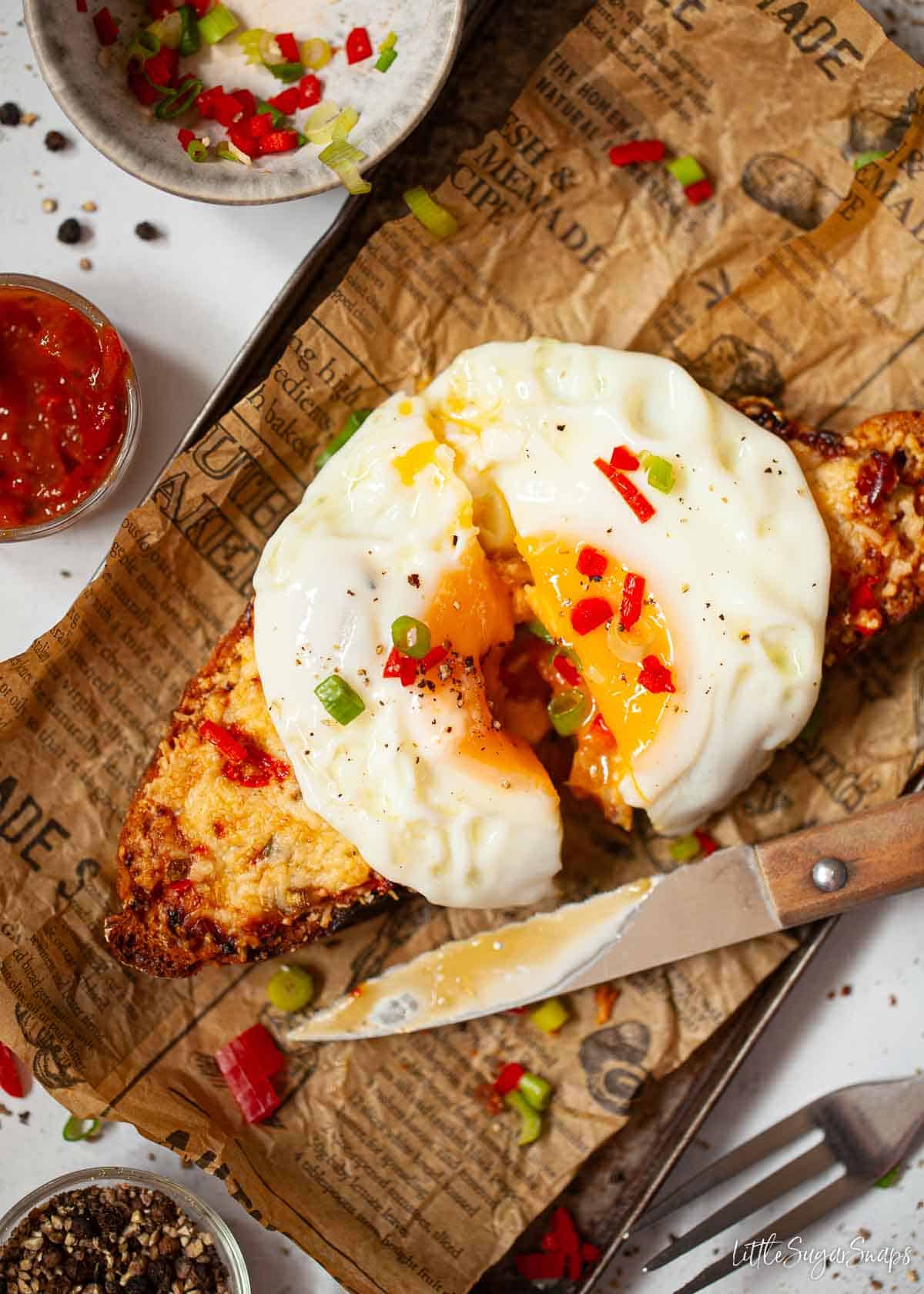 Toast topped with melted cheese, diced chilli and a fried egg that has been cut in half.