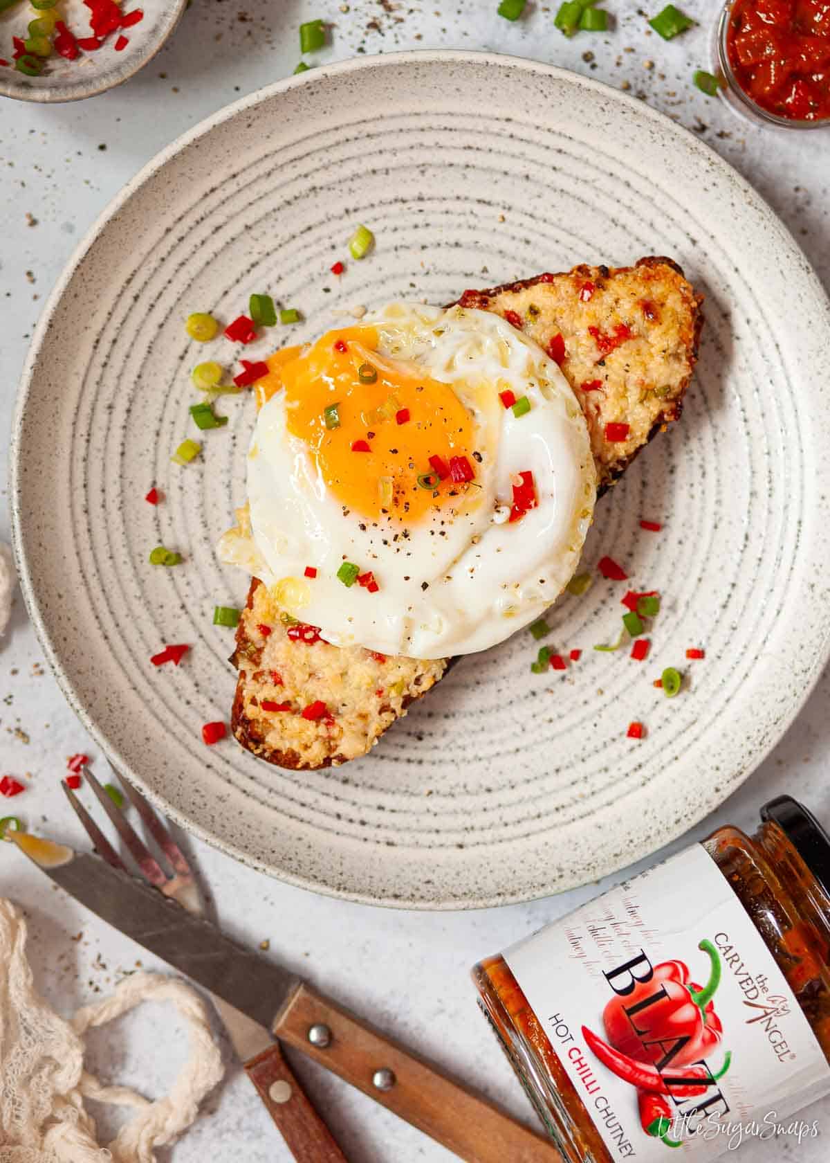 A slice of chilli cheese toast served with fried egg and garnished with red chilli and onion.