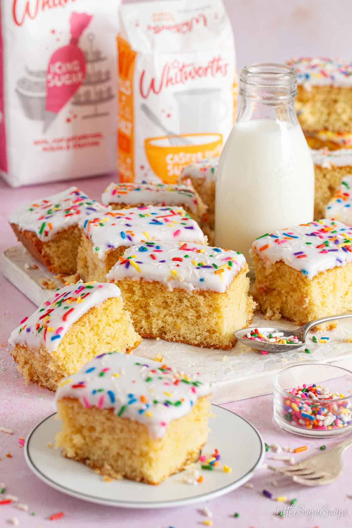 Pieces of old fashioned school cake decorated with icing and sprinkles alongside a small milk bottle.