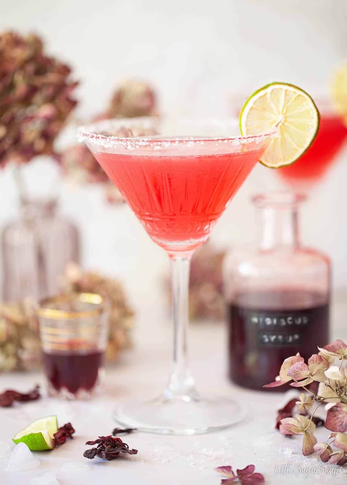 Hibiscus margarita with a bottle of hibiscus syrup in the background.