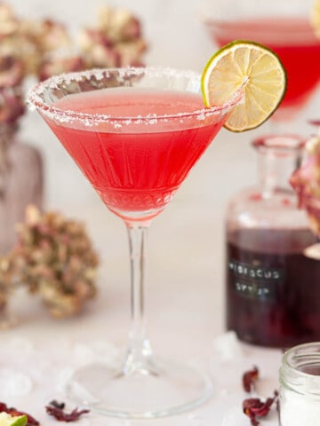 Close up of a hibiscus margarita cocktail in a salt rimmed glass with a dried lime wheel garnish.