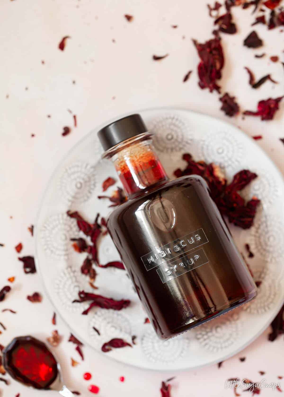 A labelled bottle of dried hibiscus flower syrup with flowers on the worktop.