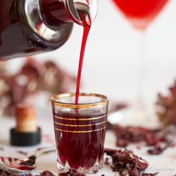 Close up of hibiscus syrup being poured from a bottle into a glass.